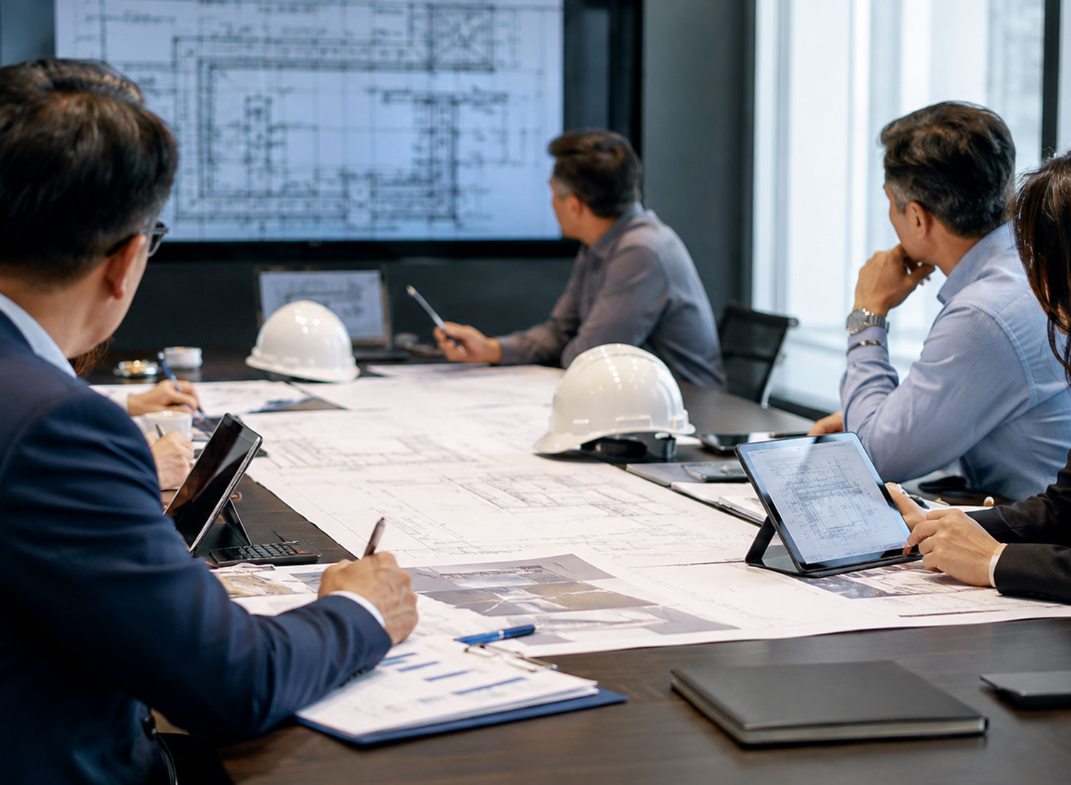 Corporate executives and First Nations partners reviewing engineering blueprints and industrial plans in a modern boardroom, highlighting asset co-ownership models in the mining and energy sector.