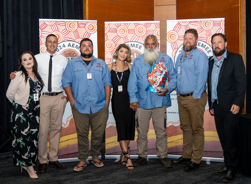 An executive panel of eight corporate leaders and community delegates standing together on stage during an industrial procurement awards event