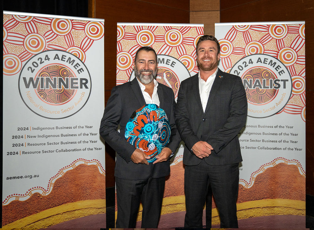 Two man standing together in formal evening wear holding a hand-painted award trophy at a business dinner.