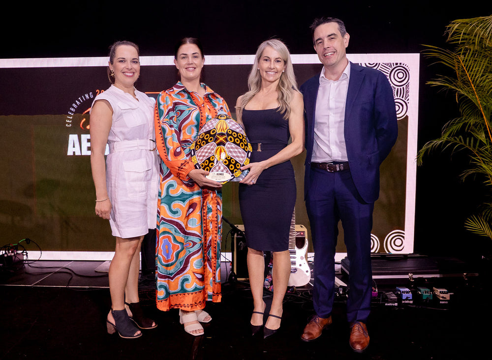 Three resource industry executives in formal business attire standing together on stage holding a handcrafted award at the AEMEE Excellence gala.