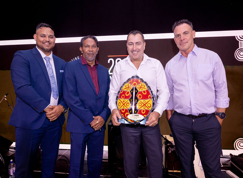 Four smiling corporate delegates standing on stage accepting a handcrafted award during the AEMEE business celebration dinner.