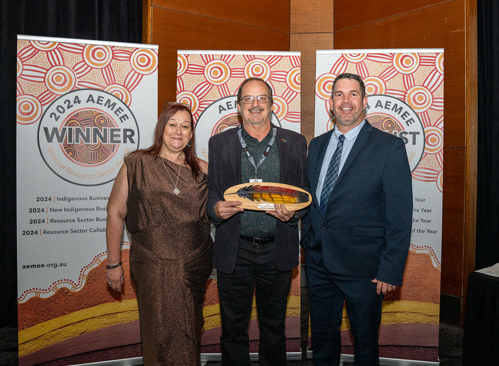 Two business leaders standing together in front of an artistic backdrop holding an industry capability award shield.