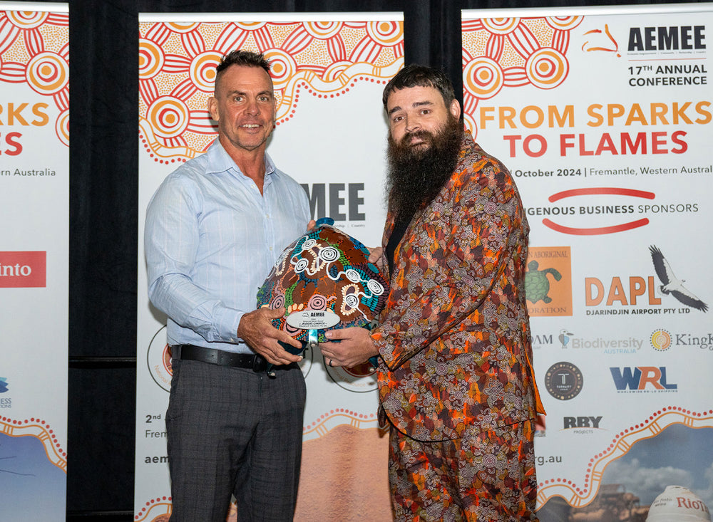 A close-up photograph of an industry leader passing a custom-designed, painted shield award to a proud recipient on stage.