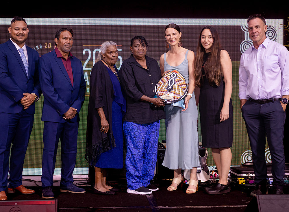 A line of six Indigenous business leaders and corporate stakeholders smiling together on stage during an evening award presentation ceremony.