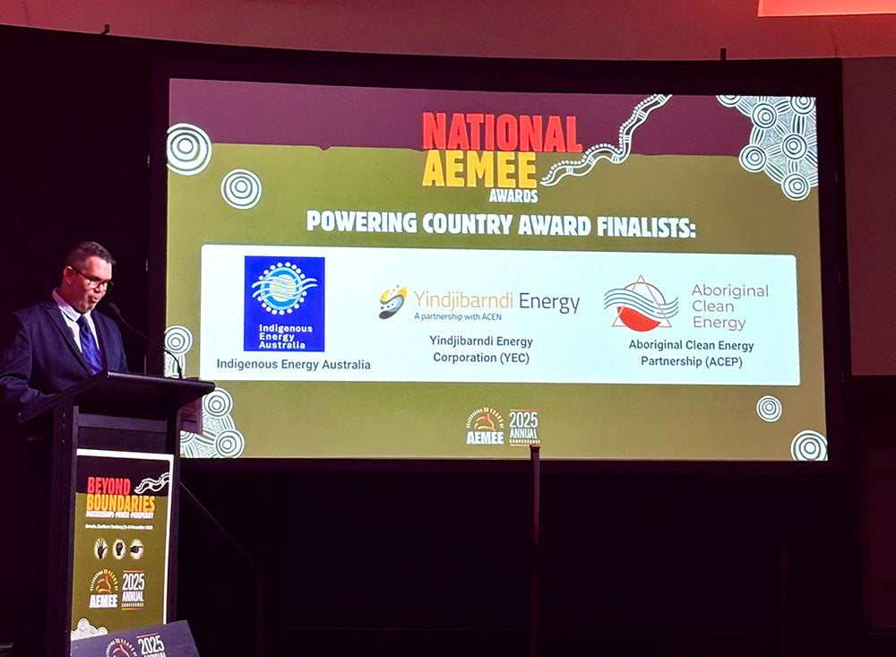 An executive corporate presenter speaking at an illuminated podium inside a large convention hall during the announcement of the national awards entries.