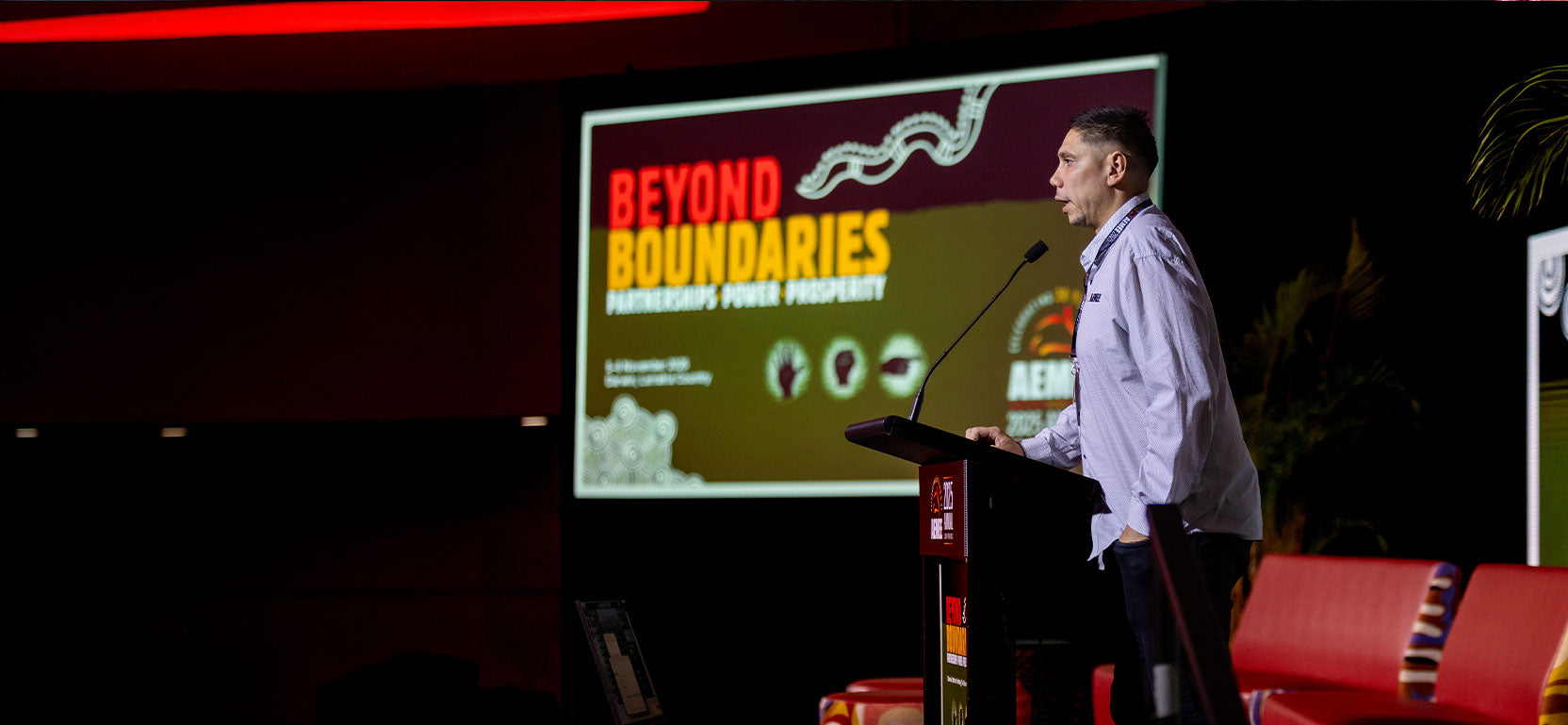 An AEMEE executive delivering a powerful national advocacy keynote at a podium in front of a large digital conference screen titled "Beyond Boundaries".