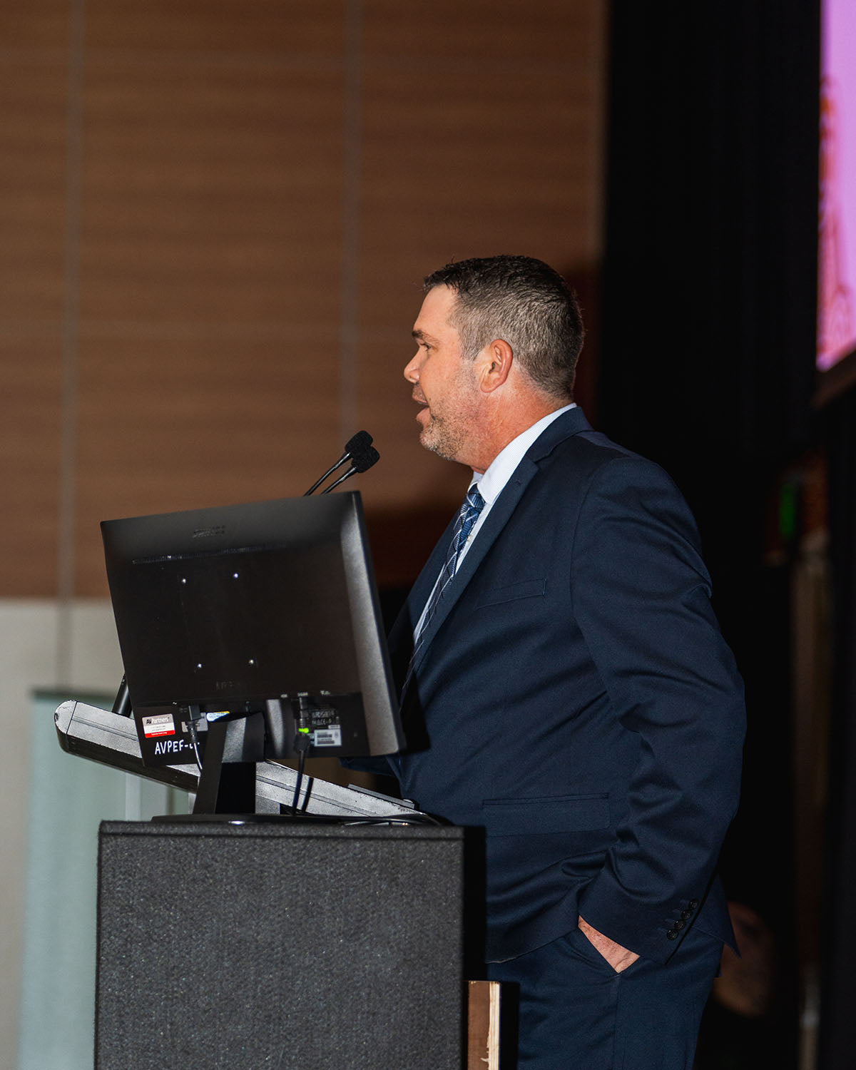 Side profile view of Brendan Bishop, Managing Director of First Enterprises, speaking into the stage microphones during the AEMEE National Resource Sector Awards ceremony.