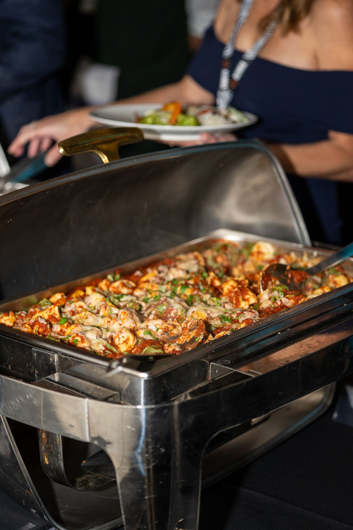 Close-up of a guest plating food from a polished stainless steel chafing dish at the gala buffet station.