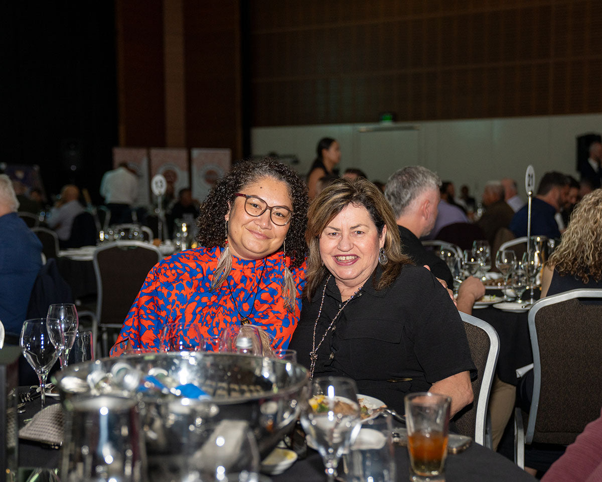 Two female conference attendees sitting at a dressed banquet table, smiling together during dinner service at the annual resources sector awards gala.