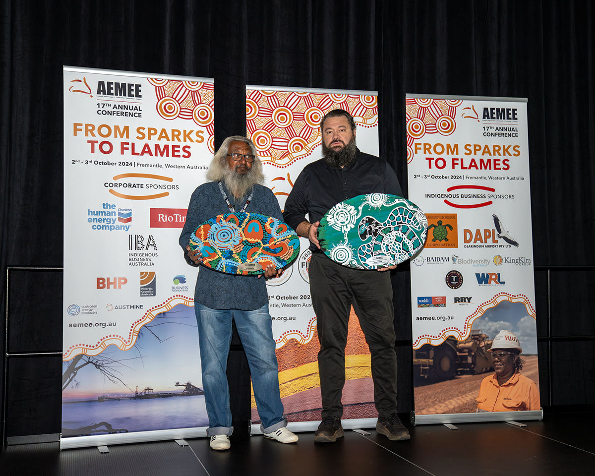 Djarindjin Aboriginal Corporation Chairman Brian Lee and CEO Nathan McIvor standing proudly on stage together while holding their large, vibrantly painted custom Indigenous artwork trophy shield.