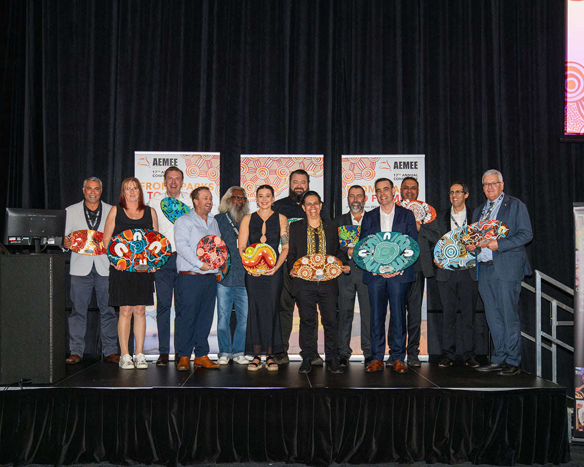 Group portrait of all the 17th Annual AEMEE National Resource Sector Award winners standing together on stage showcasing their hand-painted custom art trophies.