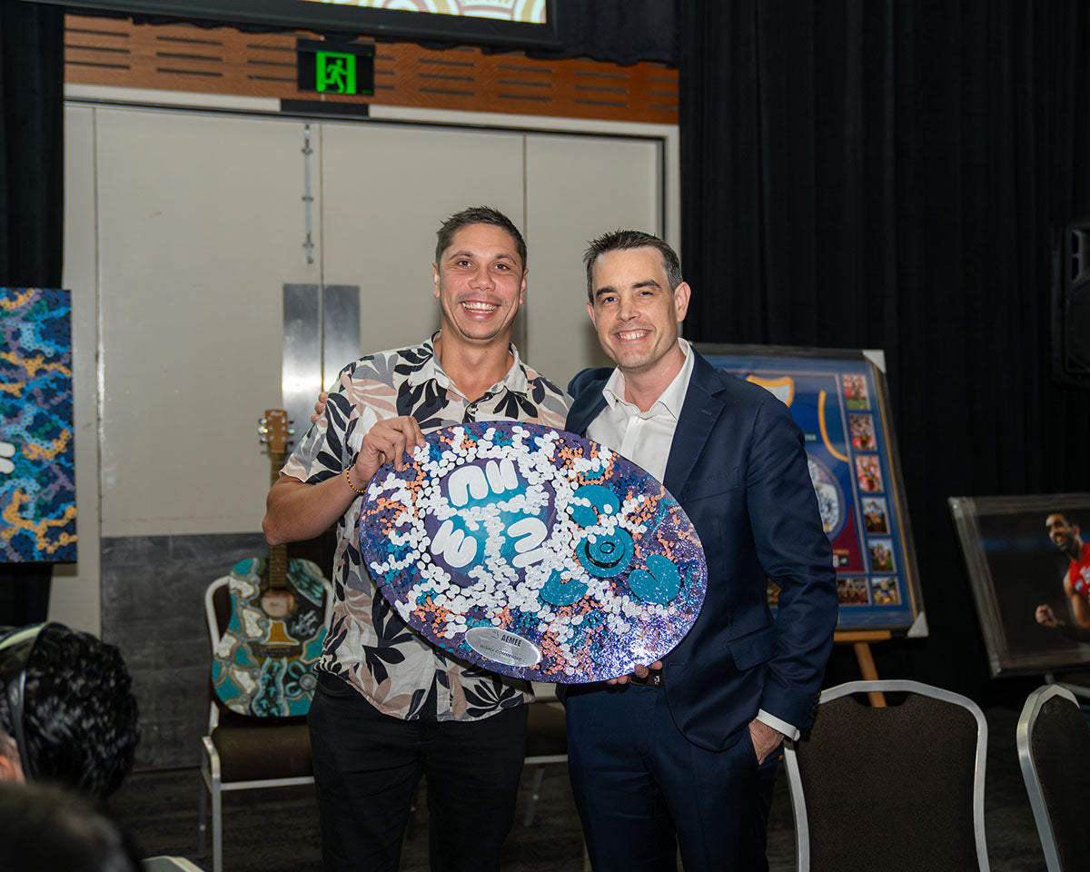 AEMEE CEO Jyi Lawton and Matt Plichta from Rio Tinto standing together and holding up a large, beautifully detailed and brightly painted custom Indigenous artwork award shield inside the gala function room.