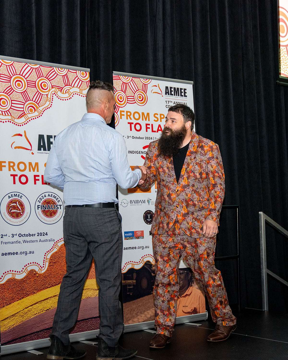 The representative from BlackRock Industries shaking hands with a corporate presenter on stage in front of the official AEMEE conference backdrop banner.
