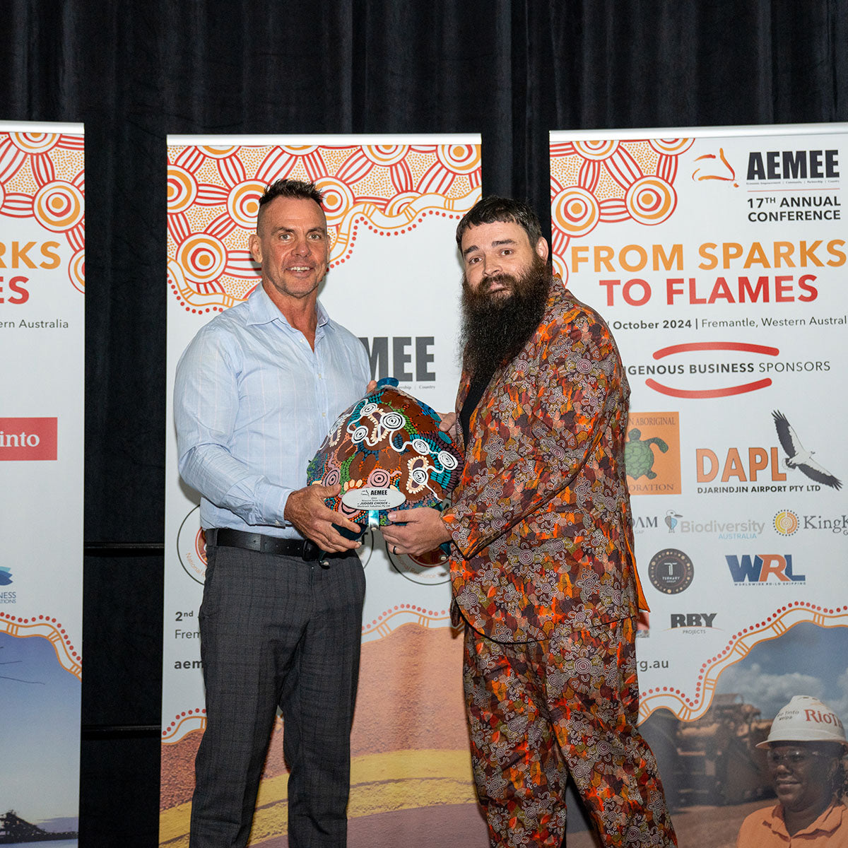 AEMEE Director Derek Flucker with the representative from BlackRock Industries, jointly holding up a vibrant custom hand-painted Indigenous art trophy shield.