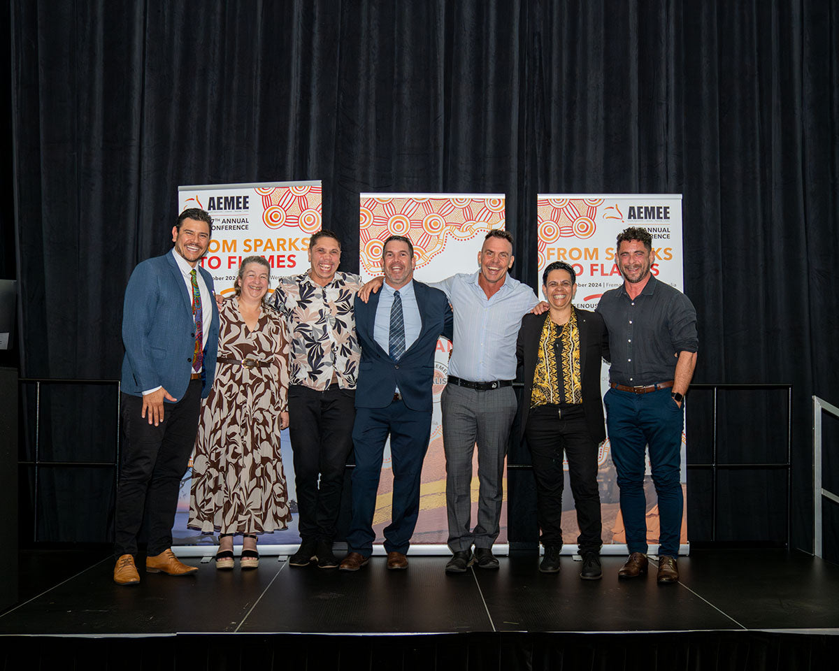 A group portrait of the AEMEE CEO and the Board of Directors standing together on stage in front of the official "From Sparks to Flames" media wall during the opening sequence of the gala night.