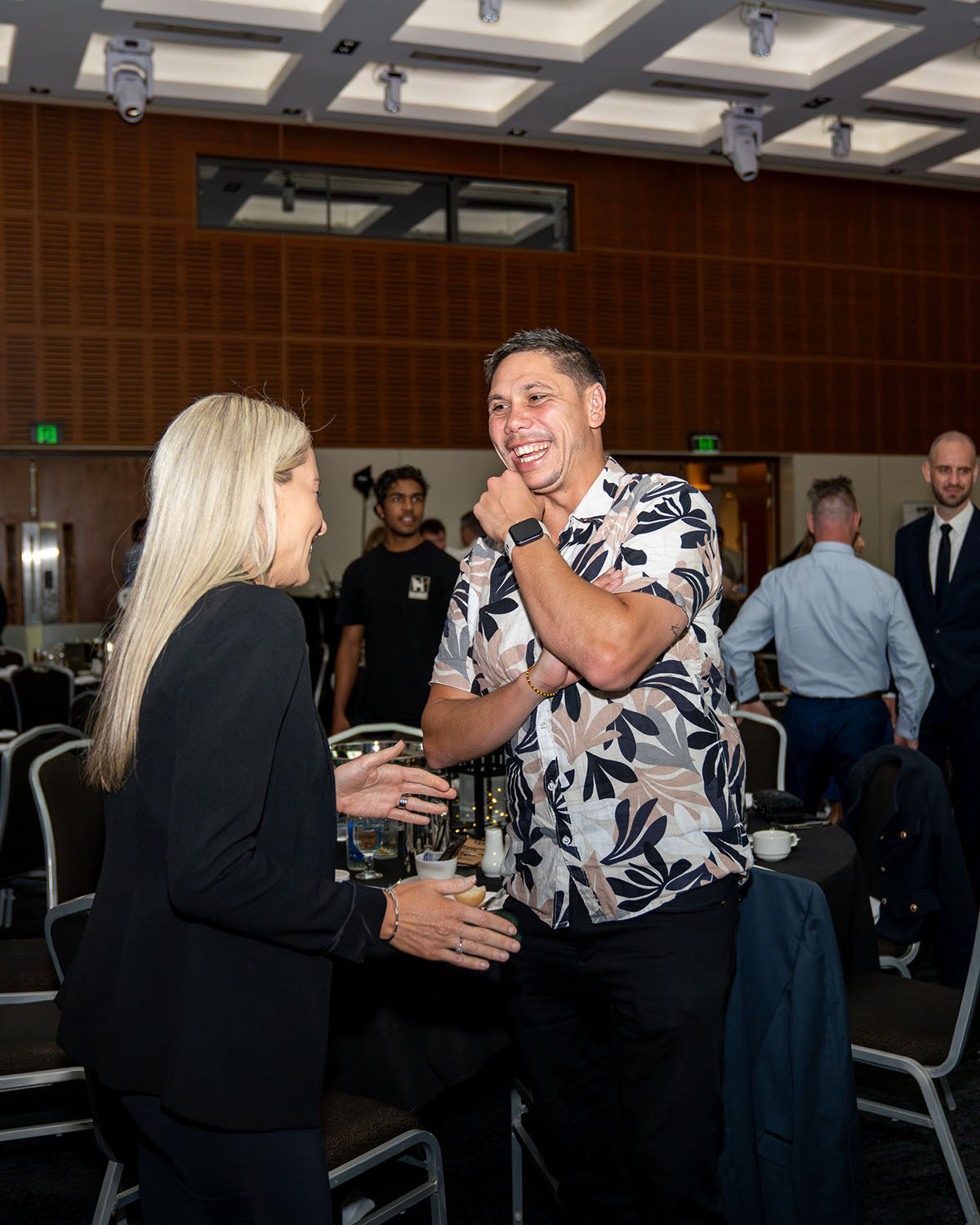 AEMEE CEO Jyi Lawton in a floral casual shirt laughing and sharing a lighthearted moment with a delegate inside the gala hall between presentations.
