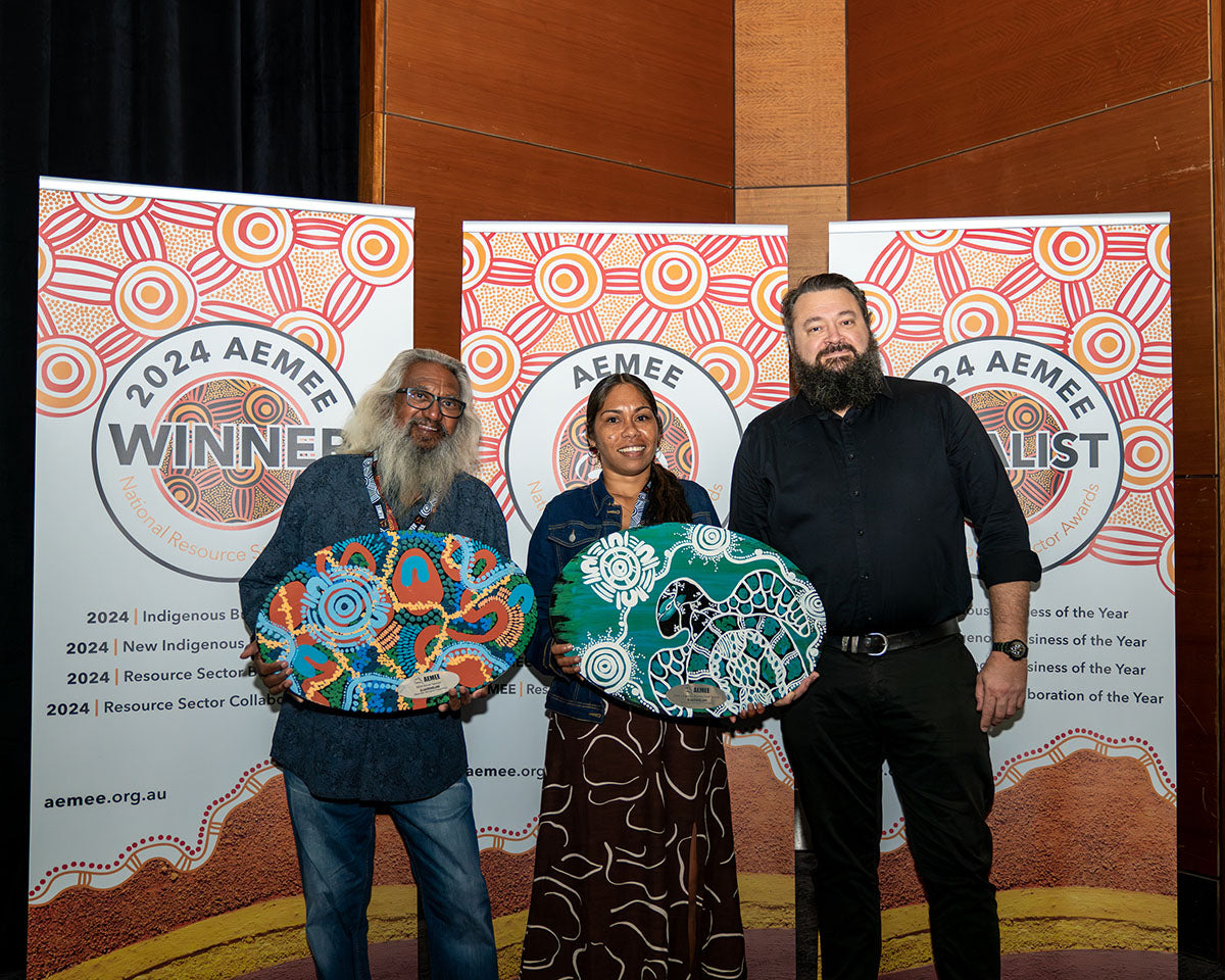 Djarindjin Aboriginal Corporation Chairman Brian Lee and CEO Nathan McIvor standing proudly in front of the media wall alongside an award presenter, holding up their two distinct hand-painted custom artwork shields.