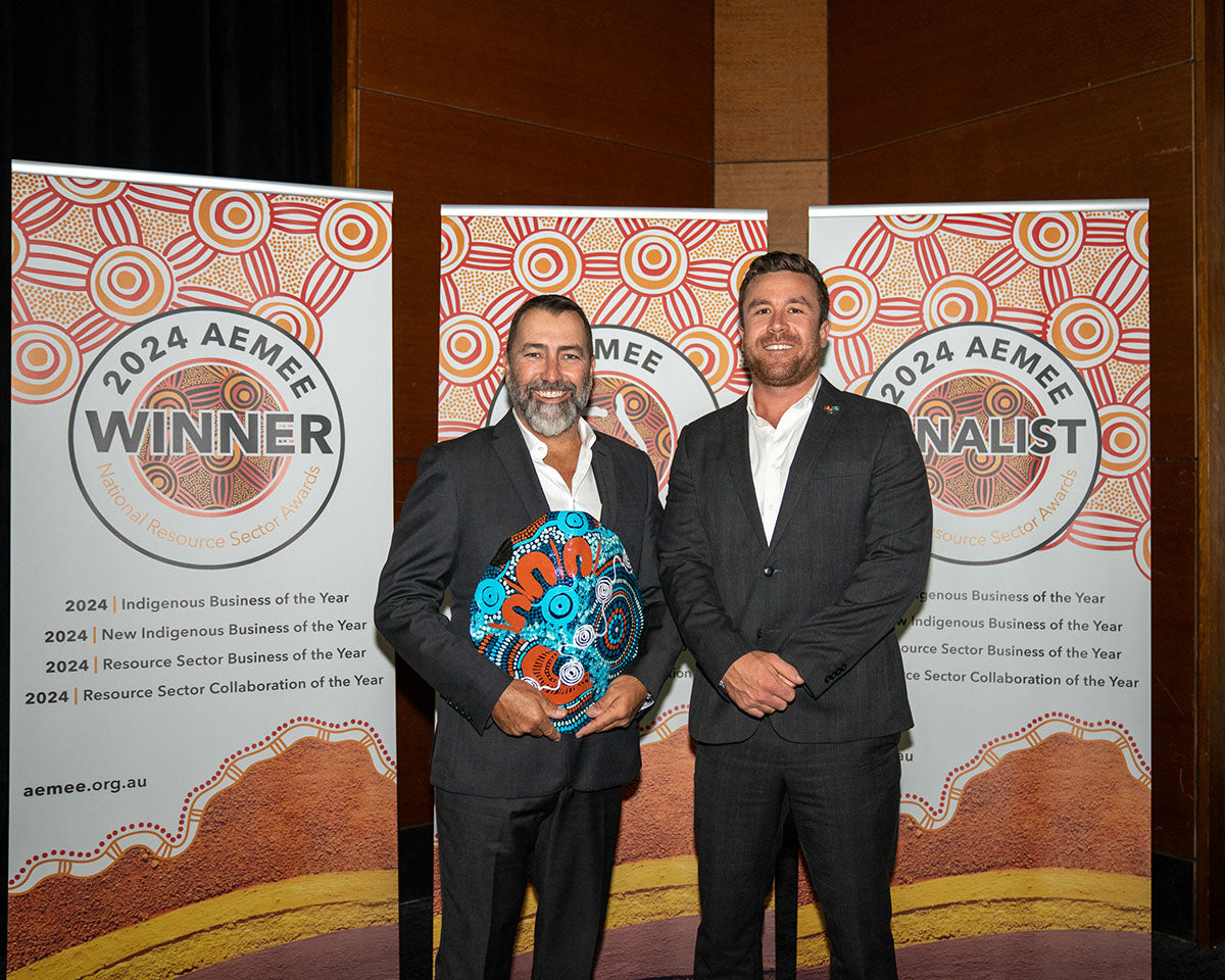 The male representative from Biodiversity Australia and QGC posing with a category presenter against the official 2024 Winner banner while proudly holding a large, blue hand-painted dot-art trophy shield.