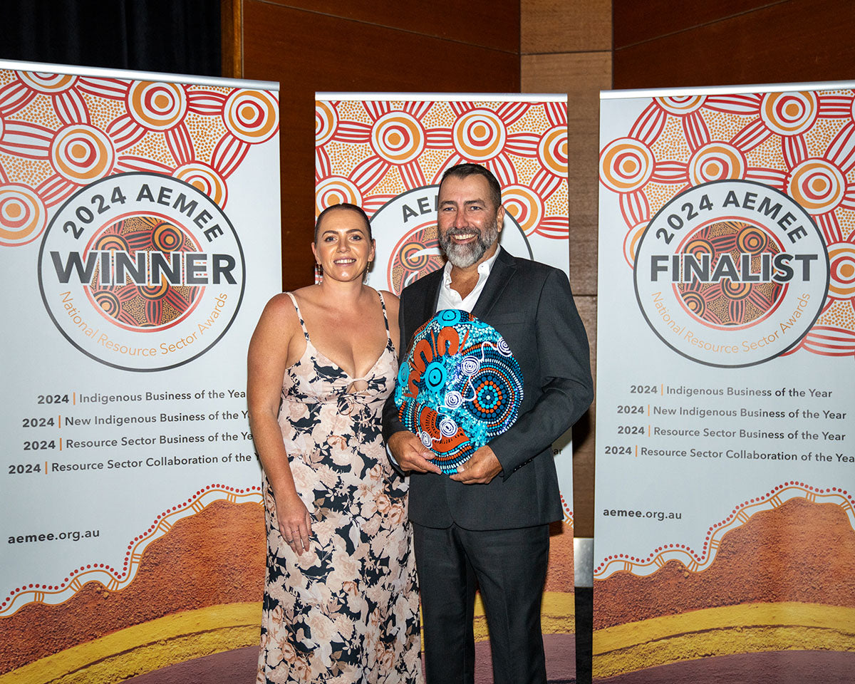 Team representatives from Biodiversity Australia and QGC standing together in front of the winner media banners, holding up their custom hand-painted oval artwork trophy for 2024 Resource Sector Collaboration of the Year.