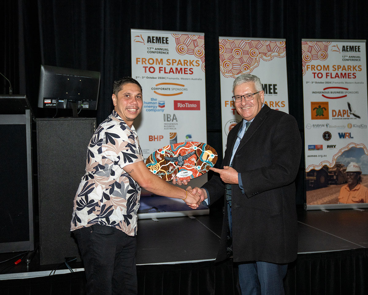 AEMEE CEO Jyi Lawton shaking hands and exchanging a custom hand-painted Indigenous art trophy shield with a representative from the Minerals Council of Australia on stage.