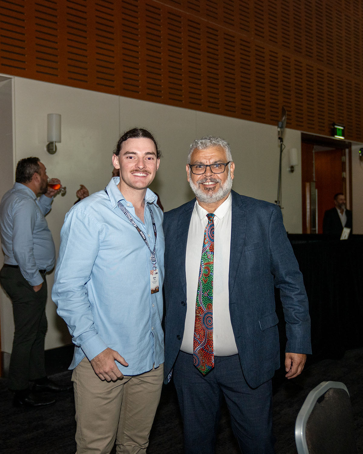 Two male corporate delegates smiling together in the auditorium lobby during a networking transition at the 17th Annual AEMEE Awards Night.