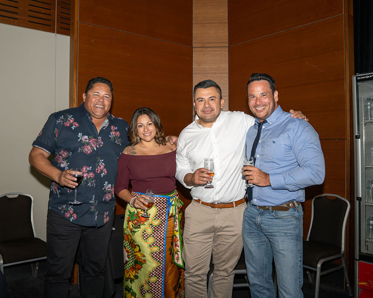 A group of four elegantly dressed industry delegates holding drinks and smiling together while social networking in the main banquet hall.