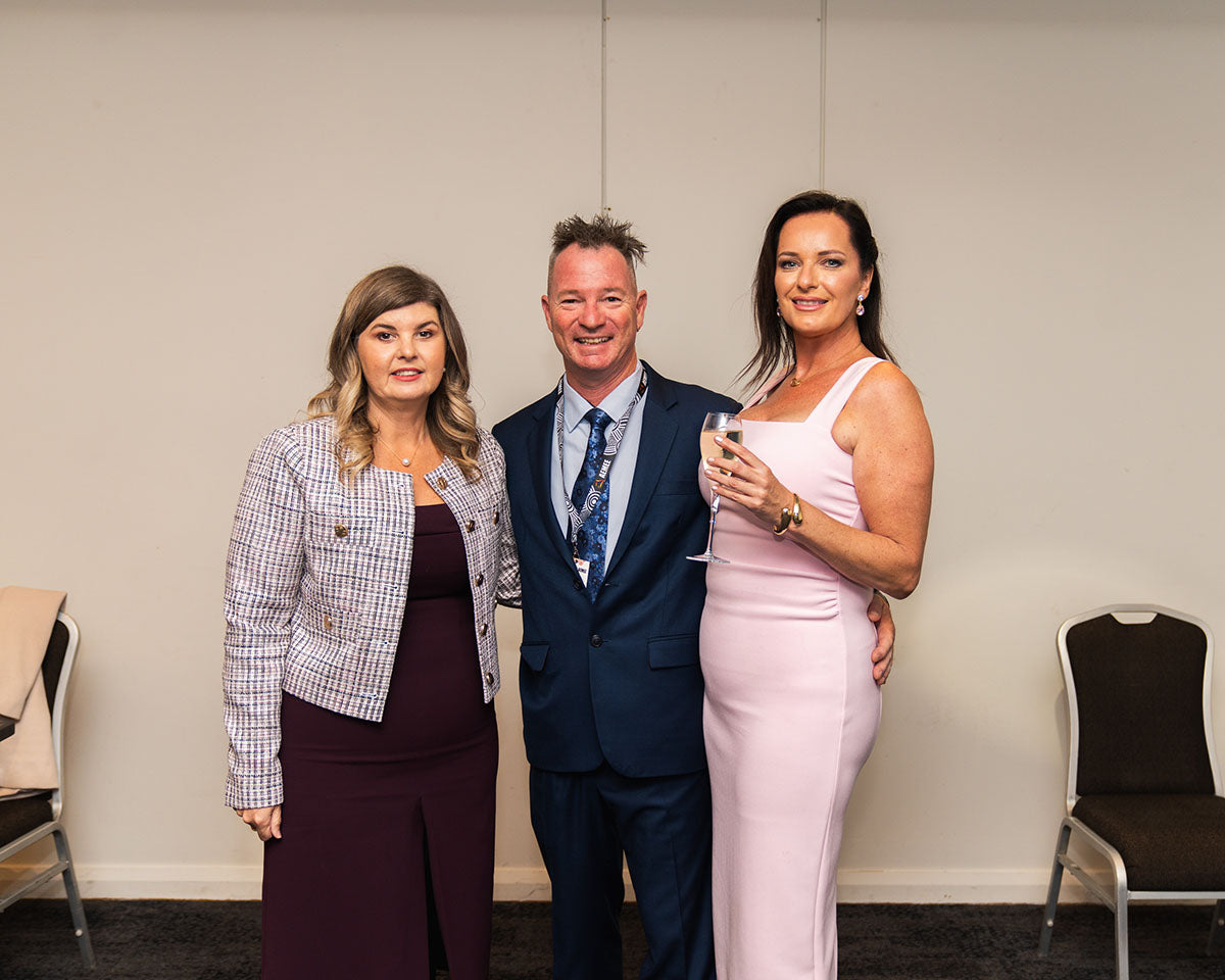 Two women and a man in formal evening wear posing together against a clean background during the gala dinner celebrations.