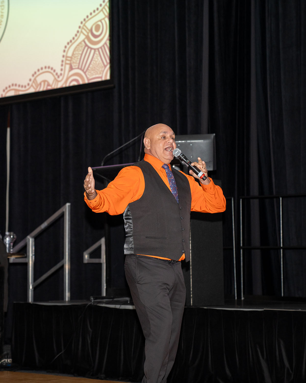 A close-up shot of comedian Kevin Kropinyeri speaking passionately into the microphone on stage during his live stand-up comedy performance at the conference gala.