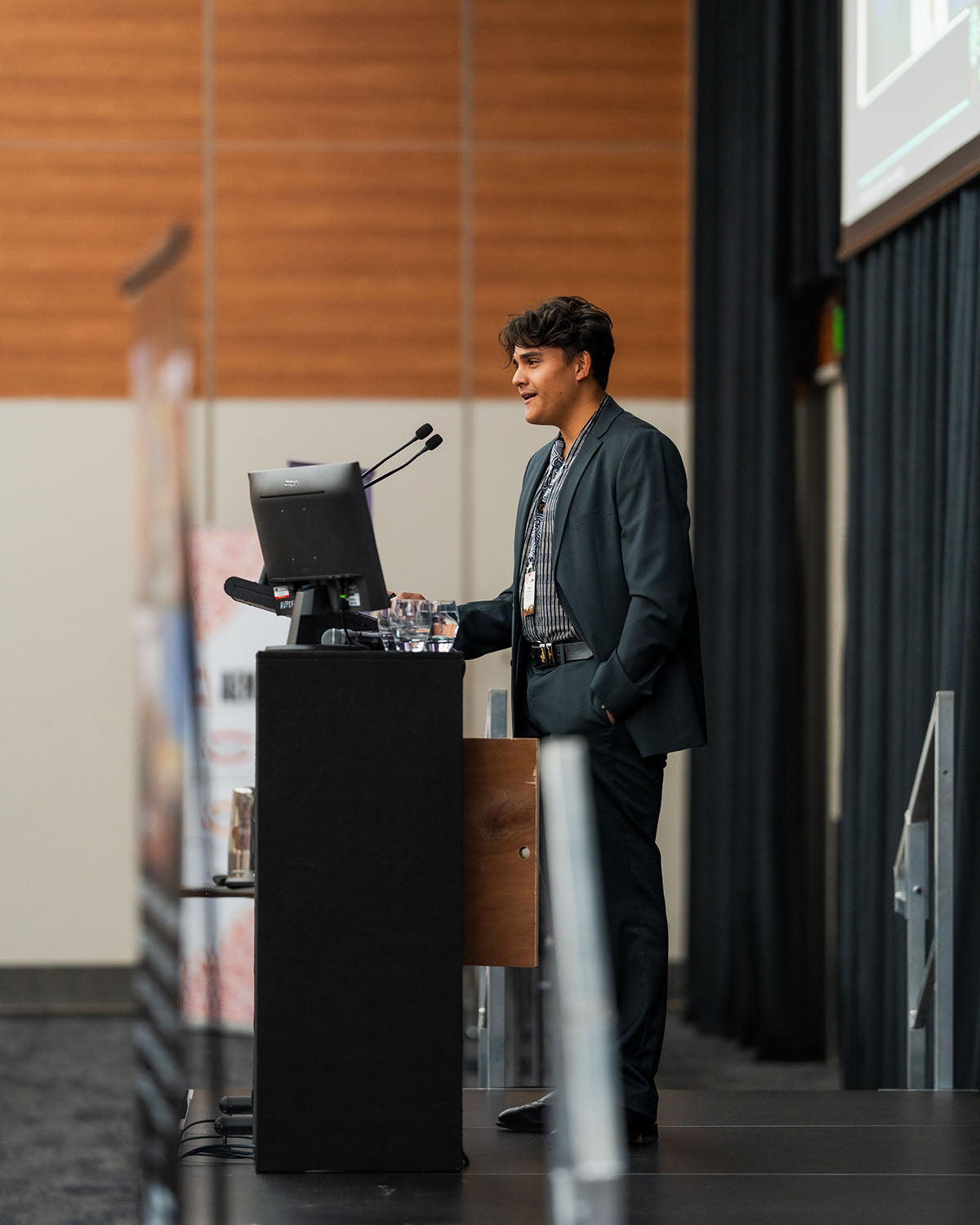 A young professional presenting from the stage microphone, highlighting strategic opportunities for youth networks at the AEMEE conference.