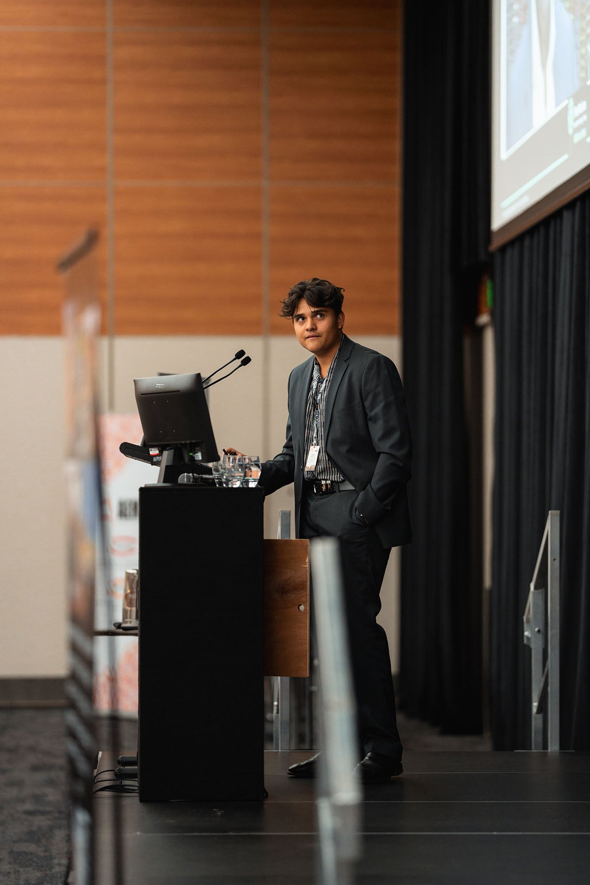A male presenter looking out at the audience from behind a main-stage podium during a supply chain breakout session at the AEMEE conference.