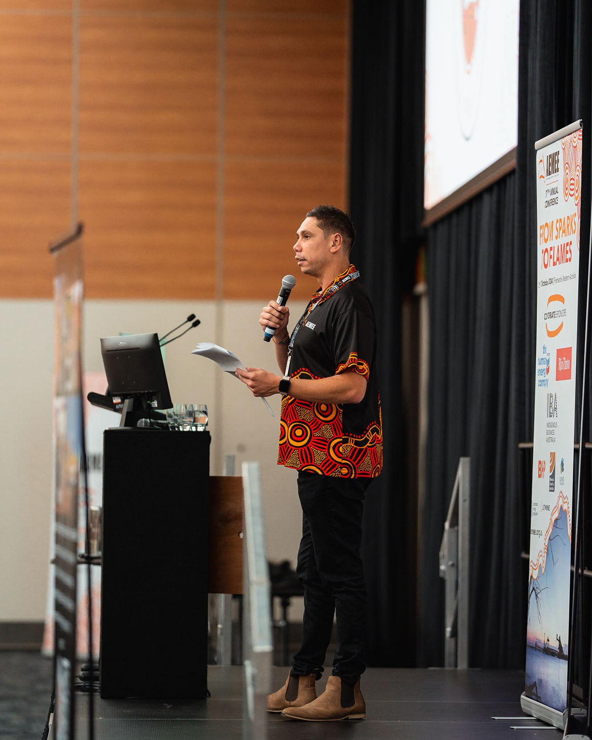 Jyi Lawton holding notes and presenting from the main stage podium during an interactive session focused on growth pathways in the Indigenous business resources sector.
