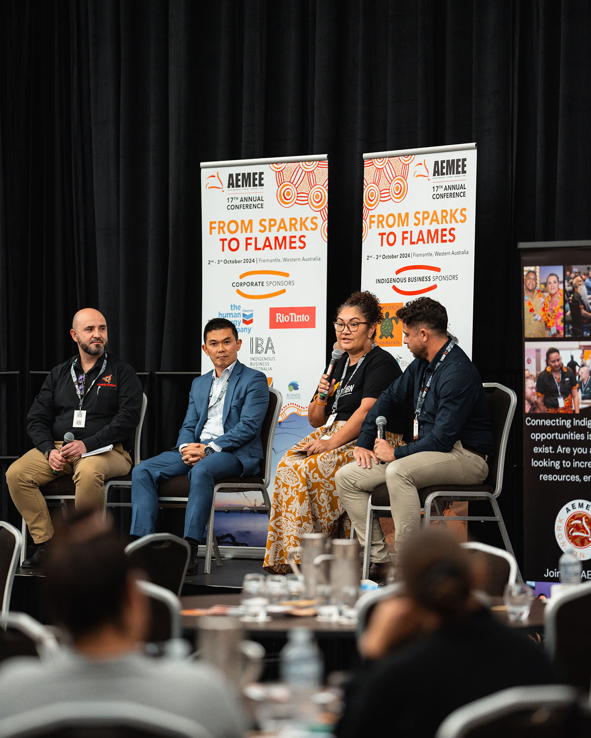 Four seated panel speakers discussing commercial opportunities on stage in front of official "From Sparks to Flames" conference media banners.