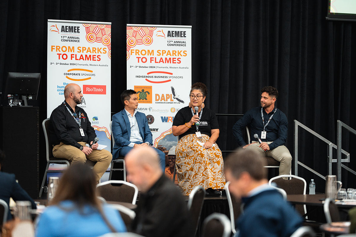 Four commercial partners sitting in front of corporate and Indigenous sponsor backdrops during a panel forum at the annual national AEMEE conference.