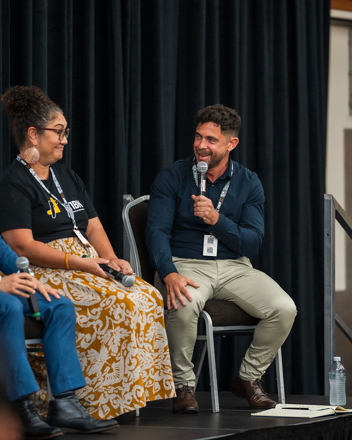 Two panel speakers sitting on stage sharing a light-hearted moment and exchanging insights on growth within the Indigenous business resources sector.