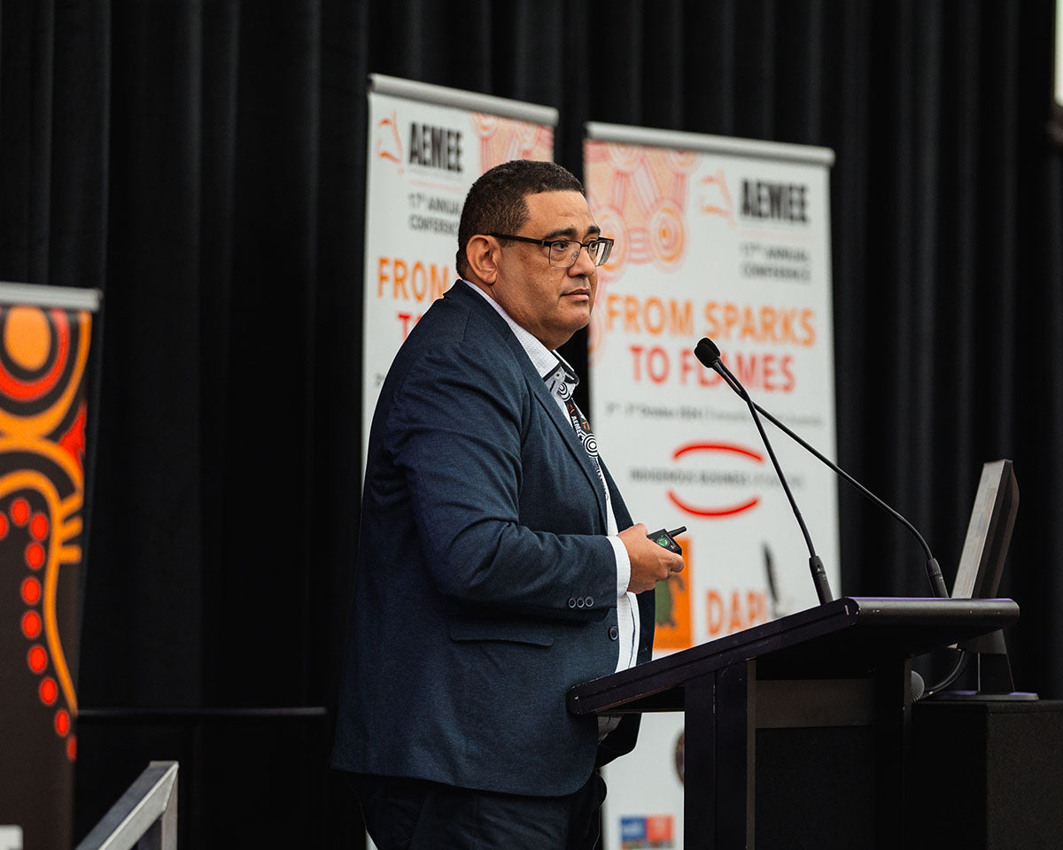 A male industry leader presenting at a stage microphone, highlighting development paths for the Indigenous business resources sector.
