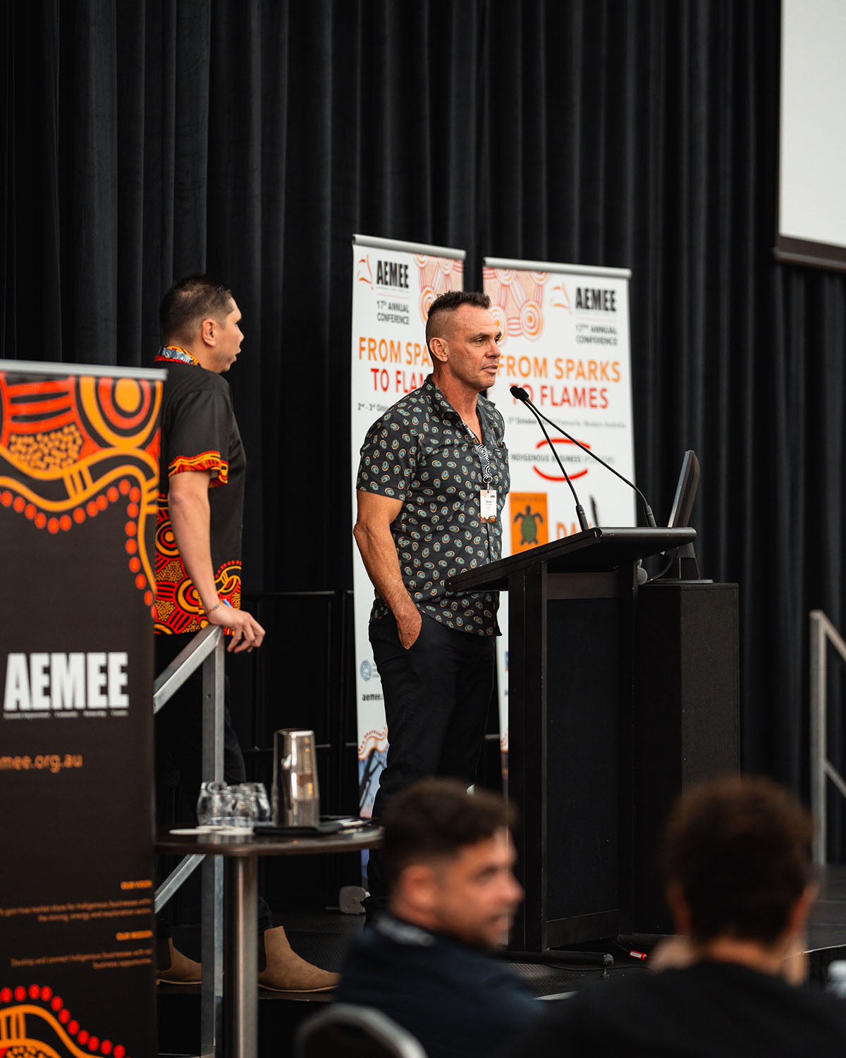 AEMEE Chairperson Derek Flucker standing at the stage podium delivering an executive address during a plenary session at the annual conference.