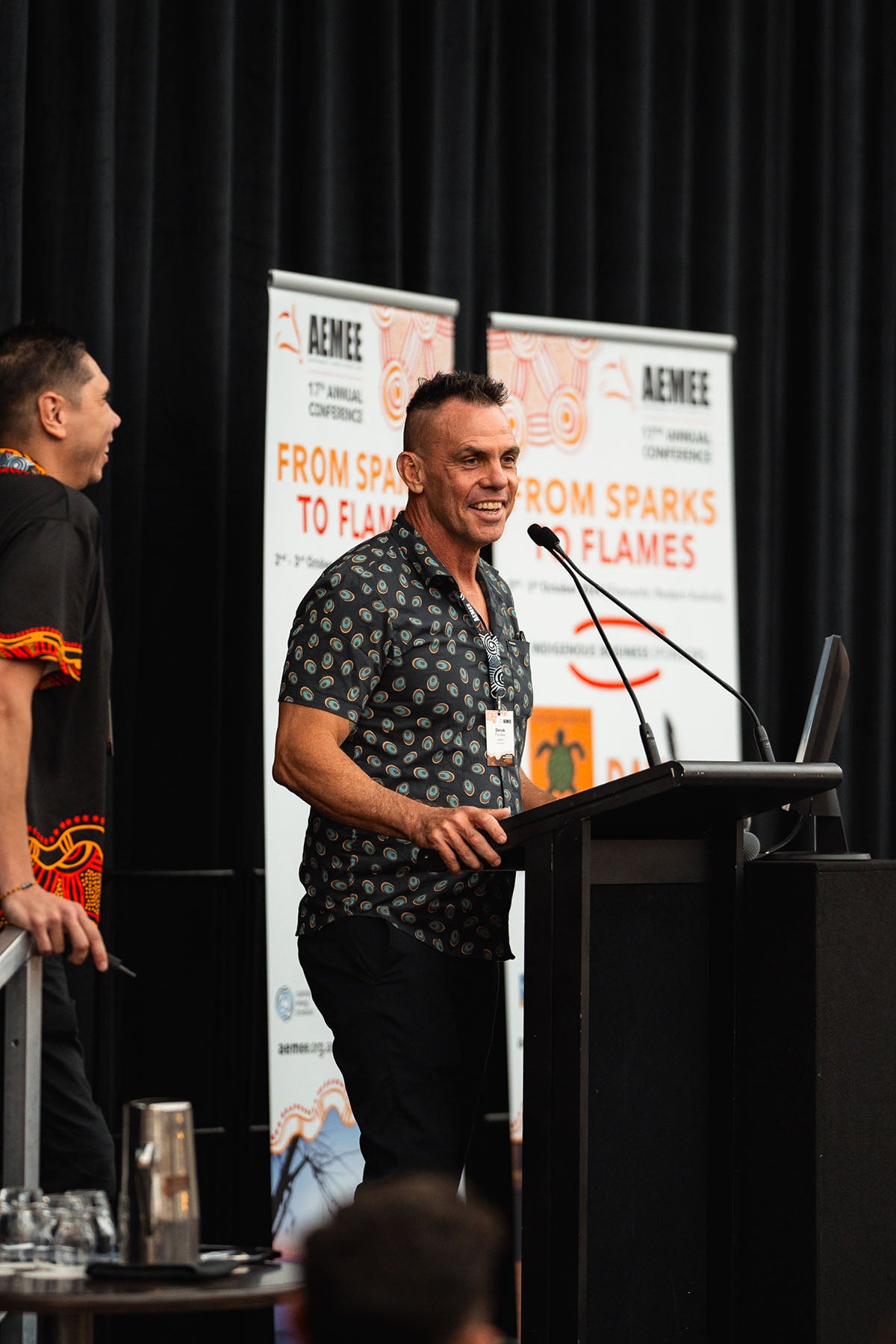 AEMEE Chairperson Derek Flucker smiles at the podium while standing alongside CEO Jyi Lawton during a leadership session tracking development in the Indigenous business resources sector.