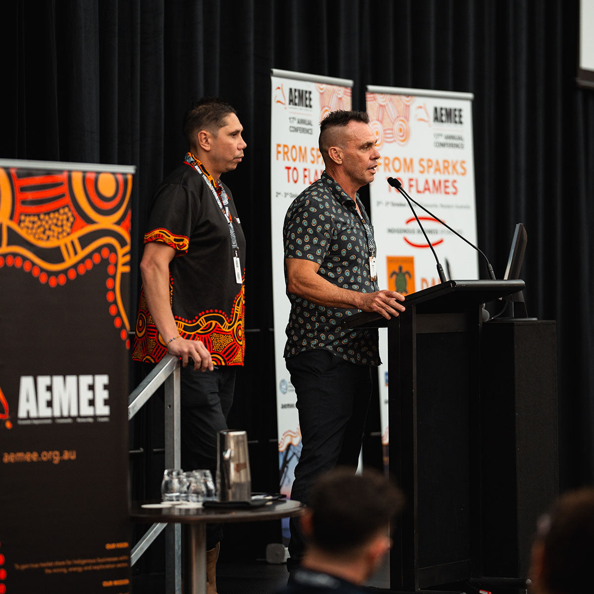 AEMEE CEO Jyi Lawton and Chairperson Derek Flucker stand together on stage during the "From Sparks to Flames" presentation at the annual national conference.
