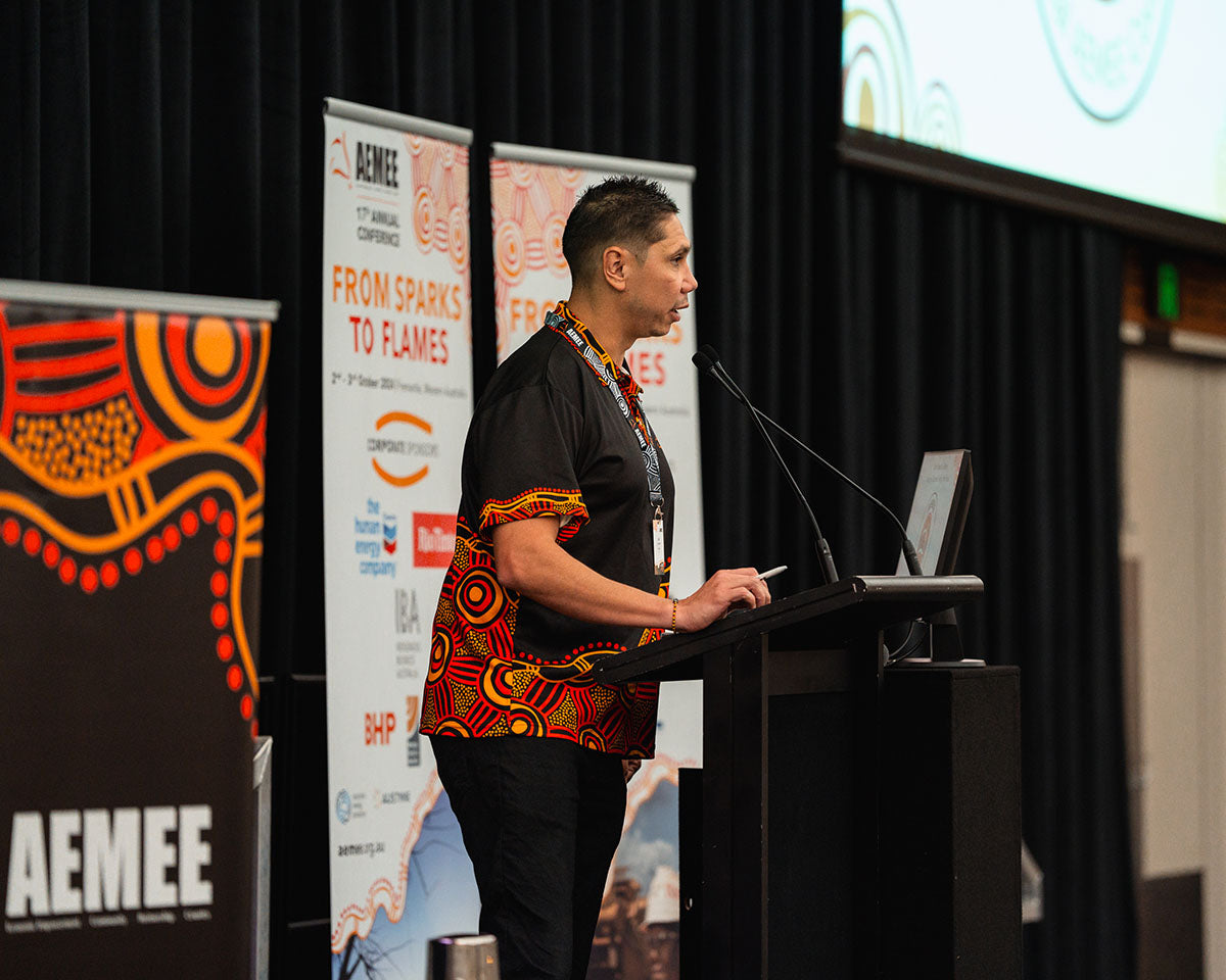 Jyi Lawton presenting from a side stage angle in front of an official corporate media banner highlighting growth pathways in the Indigenous business resources sector.