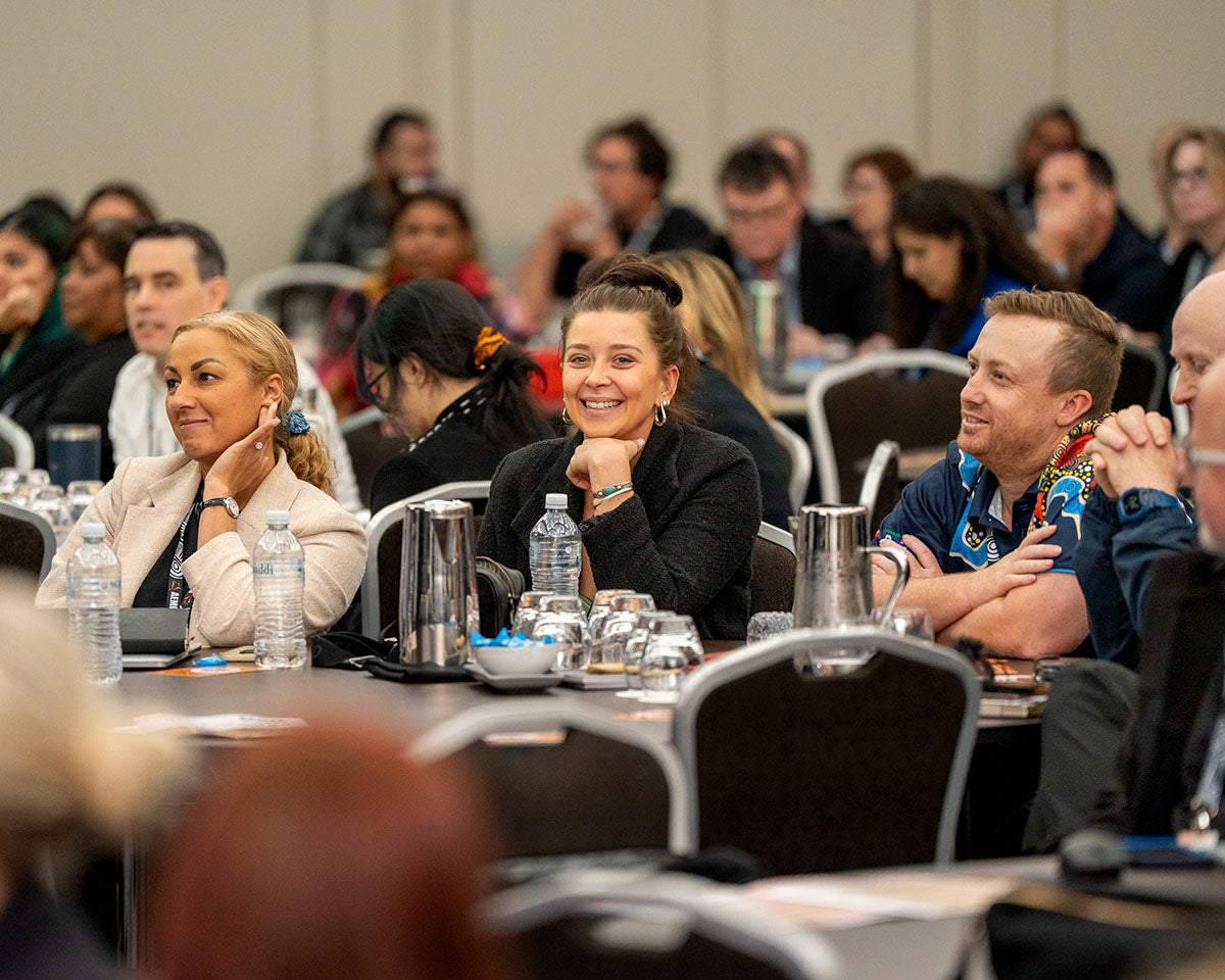 Smiling corporate attendees and industry delegates listening intently from their tables during a keynote session at the annual AEMEE conference.