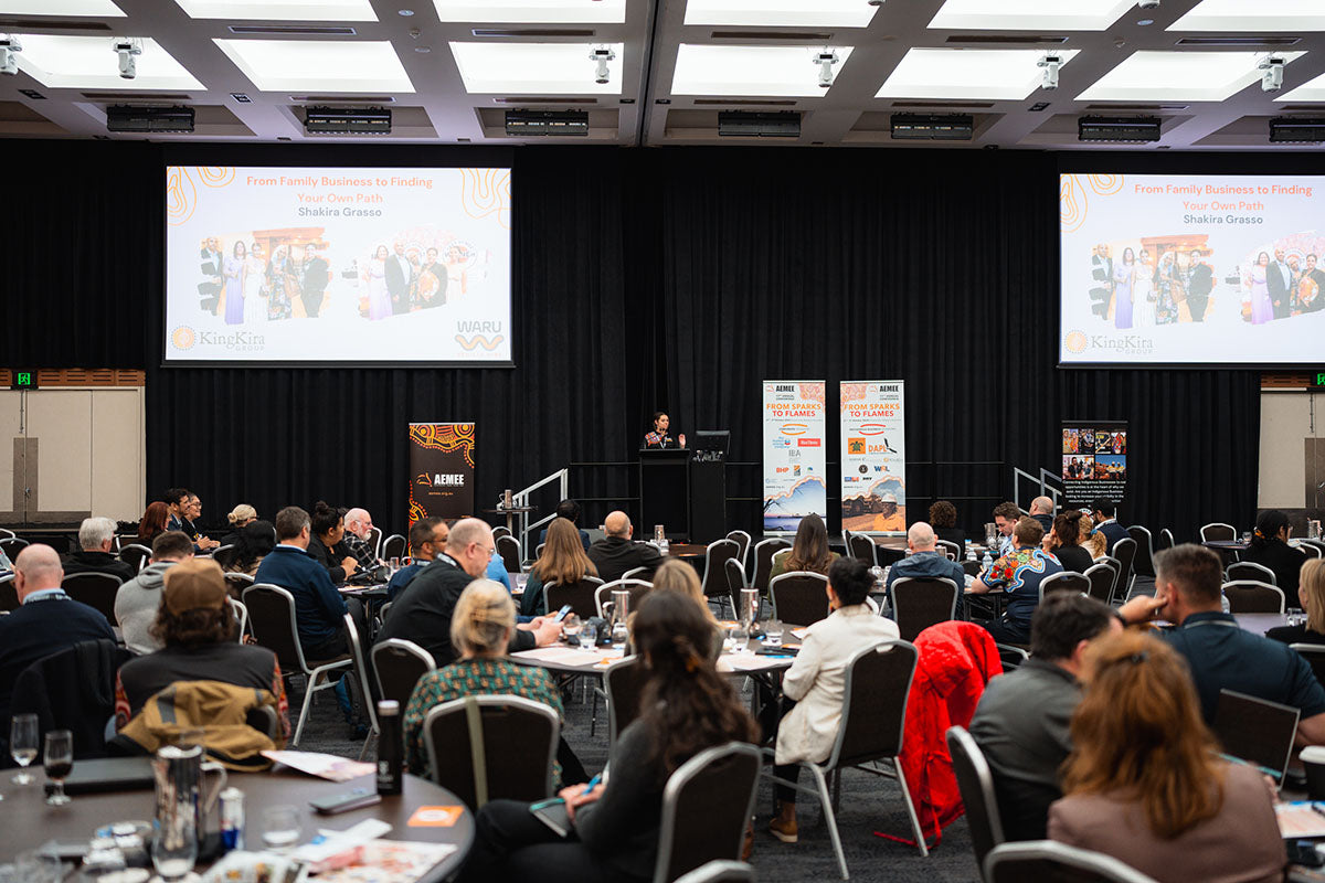 An overhead view of a fully packed presentation hall with seated industry delegates watching a keynote projector screen during a plenary panel at the AEMEE conference.