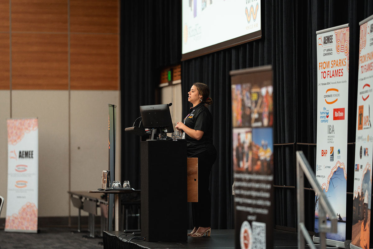 A female industry representative presenting at the stage podium during an opening keynote session at the annual national AEMEE conference.