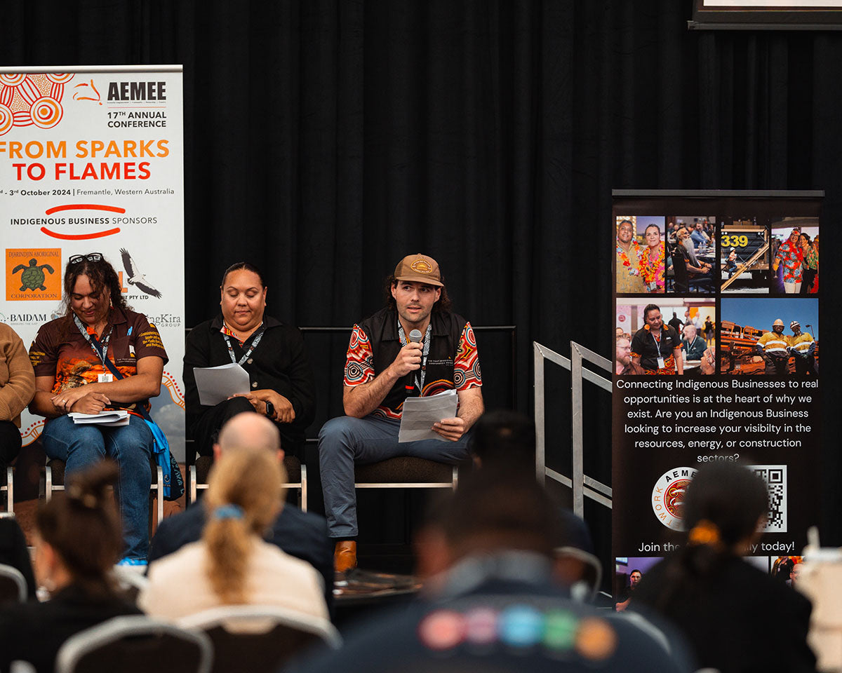 A male panelist wearing a cap and traditional print shirt speaks into a microphone on stage during a youth breakout session at the annual AEMEE conference.