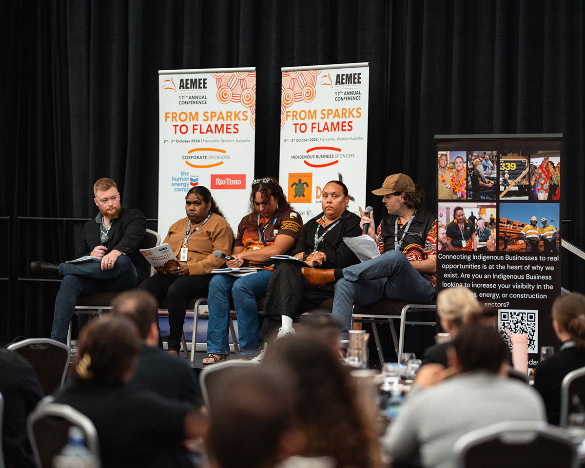 Five seated panelists on stage addressing a corporate audience during the "From Sparks to Flames" plenary session at the national AEMEE conference.