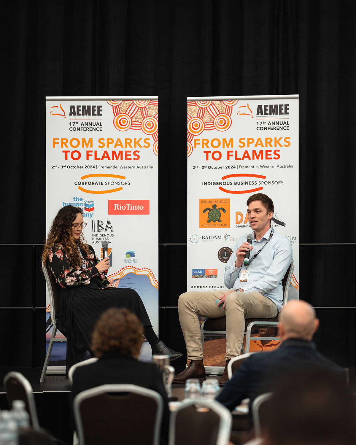 Two panelists presenting on stage backdropped by official "From Sparks to Flames" corporate sponsor media banners at the annual national AEMEE conference.
