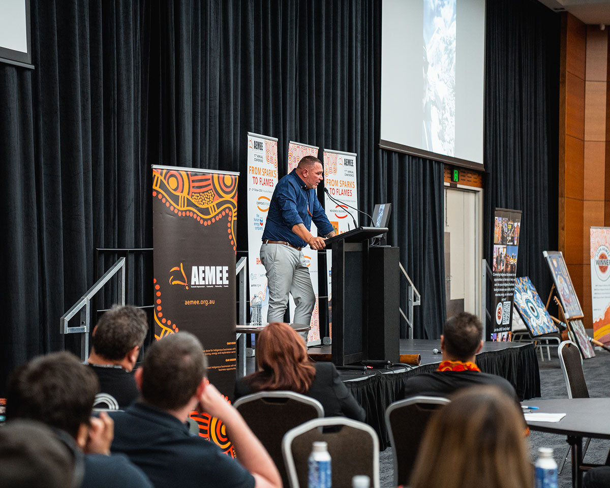 Seated audience delegates looking towards the stage as a presenter delivers a closing address on strategic development pathways within the Indigenous business resources sector.
