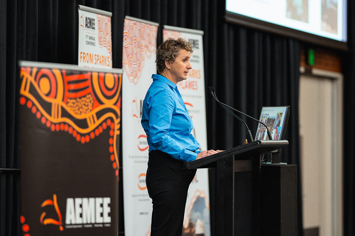 Keynote speaker Susan O'Byrne presenting from the stage podium during the 17th Annual AEMEE conference, focusing on financial pathways for Indigenous businesses and community.