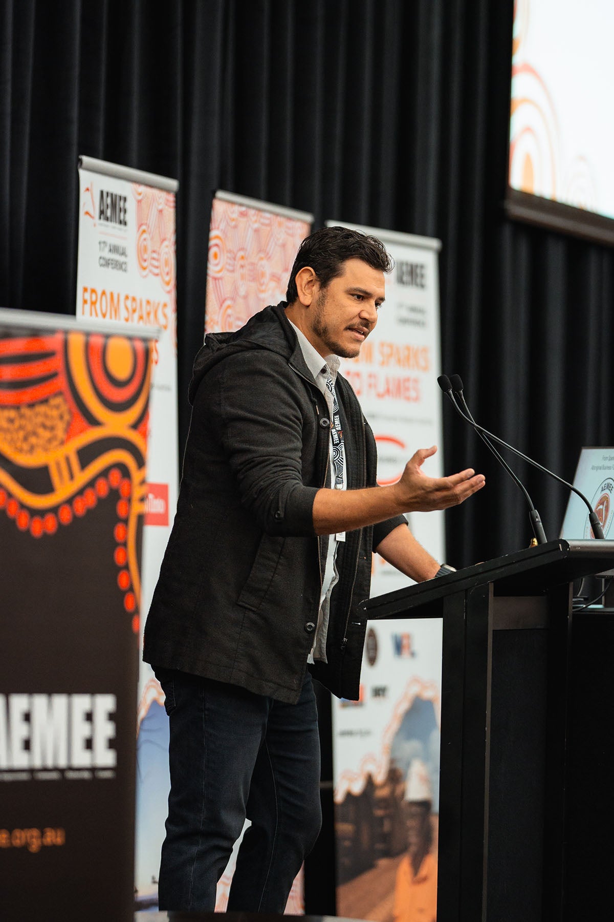 DICE Australia Director Raymond Pratt speaking with hand gestures at the stage microphone during an interactive forum focused on the Indigenous business resources sector.