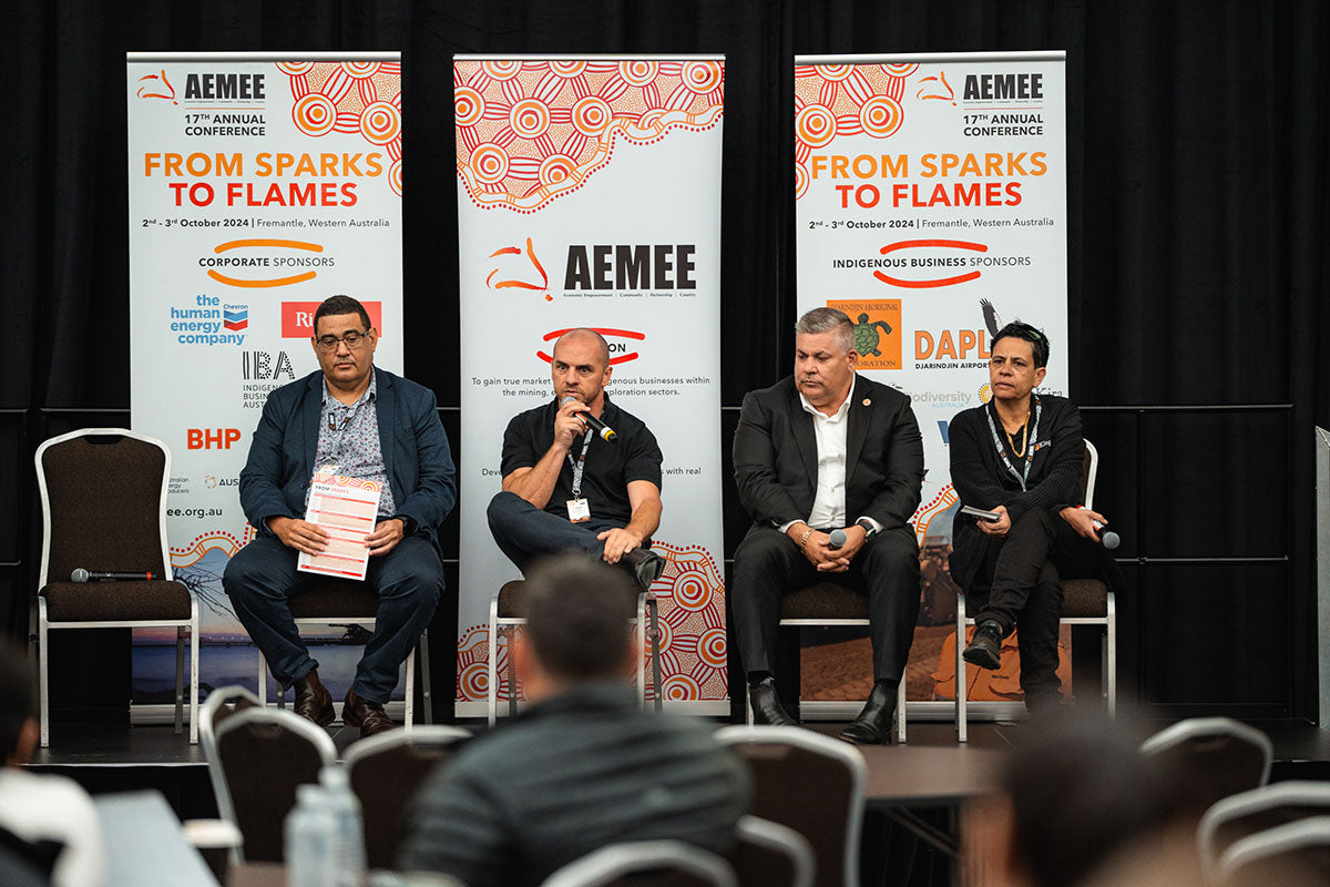 Four panel speakers seated in front of official corporate media banners, addressing the audience at the 17th Annual AEMEE conference.