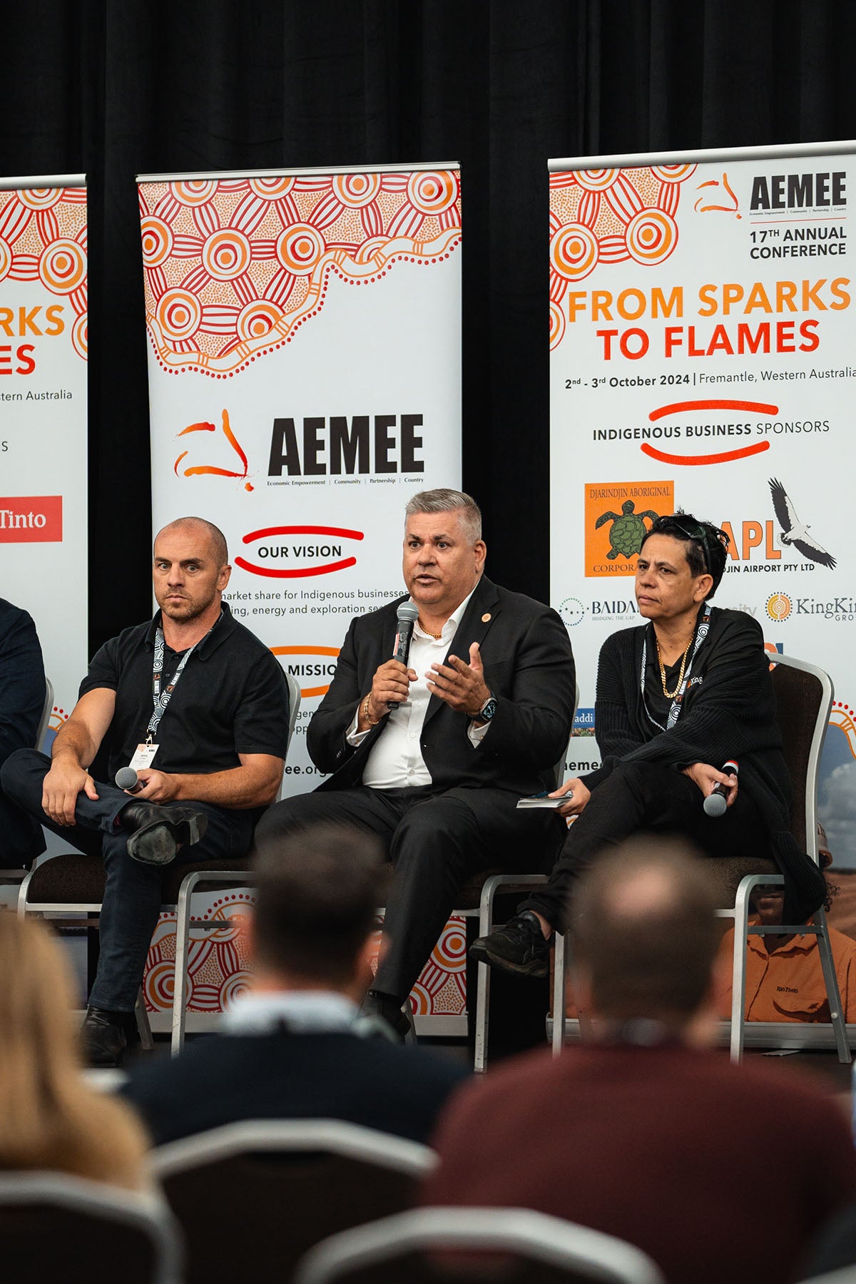 A male industry panelist speaking into a microphone while seated alongside other commercial partners beneath an official AEMEE vision graphic.